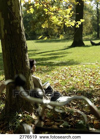 Stock Photo - Rear view of mature woman resting against tree . Fotosearch