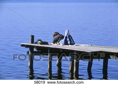 Stock Photo - Rear view of teenage girl lying on pier . Fotosearch
