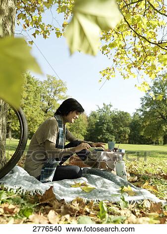 Stock Image - Side profile of mature woman applying cheese on slice in park . Fotosearch
