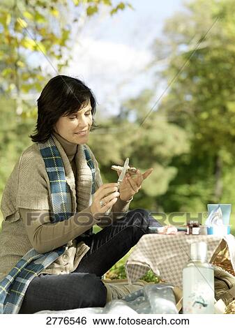Stock Photograph - Side profile of mature woman applying cheese on slice of bread in park . Fotosearch