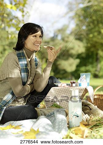 Picture - Side profile of mature woman eating a cheese slice in park . Fotosearch