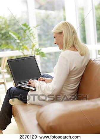 Stock Photo - Side profile of woman using laptop on couch . Fotosearch