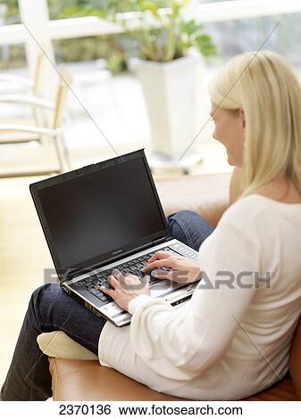 Stock Photograph - Side profile of woman using laptop on couch . Fotosearch
