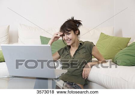 Stock Photo - Smiling woman in living room looking at laptop . Fotosearch