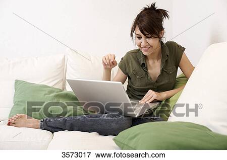 Stock Photo - Smiling woman in living room with laptop . Fotosearch