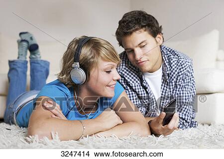 Teenager couple lying on carpet and listening to music, low-angle view View Large Photo Image Picture - Teenager couple lying on carpet and listening to music, low-angle view . Fotosearch