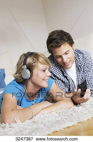 Stock Photo - Teenager couple lying on carpet and listening to music, low-angle view . Fotosearch