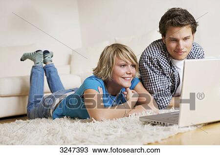 Teenager couple lying on carpet, watching media on notebook, low-angle view View Large Photo Image Stock Image - Teenager couple lying on carpet, watching media on notebook, low-angle view . Fotosearch