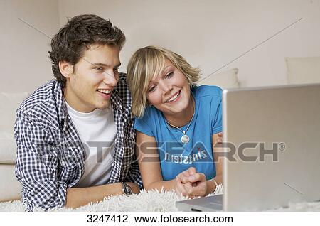 Stock Image - Teenager couple lying on carpet, watching media on notebook, low-angle view . Fotosearch