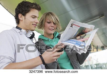 Teenager couple reading newspaper on the go, view from below View Large Photo Image Stock Photograph - Teenager couple reading newspaper on the go, view from below . Fotosearch