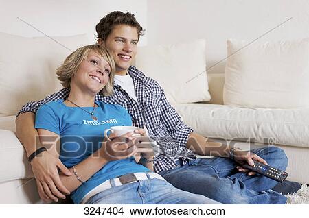 Teenager couple sitting in front of couch and watching television, horizontal format View Large Photo Image Picture - Teenager couple sitting in front of couch and watching television, horizontal format . Fotosearch