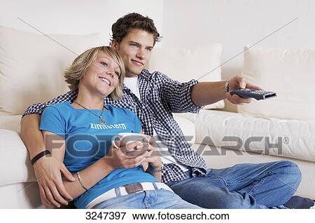 Stock Photo - Teenager couple sitting in front of couch and watching television, horizontal format . Fotosearch