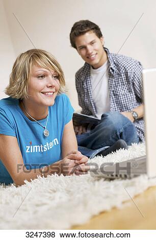 Stock Photo - Teenager couple using media in living room, slanted view . Fotosearch