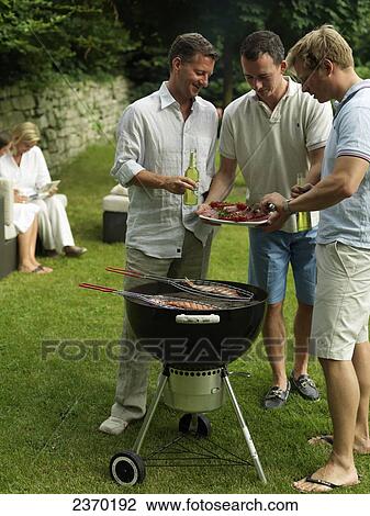 Stock Image - Three men preparing fish on barbeque grill in garden . Fotosearch