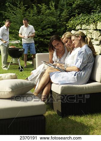 Stock Image - Three women looking at photo albums on couch . Fotosearch