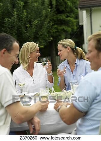 Stock Image - Two couples smiling at garden table . Fotosearch