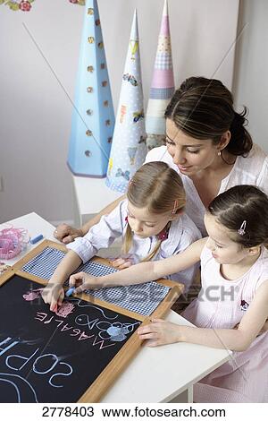 Two girls writing on chalkboard with their mother sitting behind them View Large Photo Image Stock Image - Two girls writing on chalkboard with their mother sitting behind them . Fotosearch
