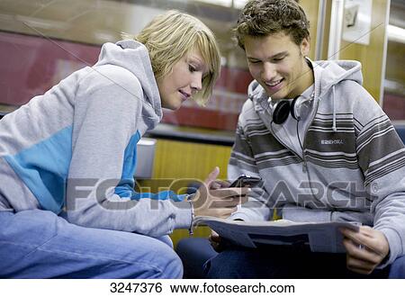 Two teenagers using mobile phone and print media in city train, slanted view View Large Photo Image Stock Photograph - Two teenagers using mobile phone and print media in city train, slanted view . Fotosearch