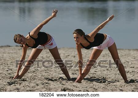 Picture - Two young women doing fitness exercises at beach, full shot . Fotosearch