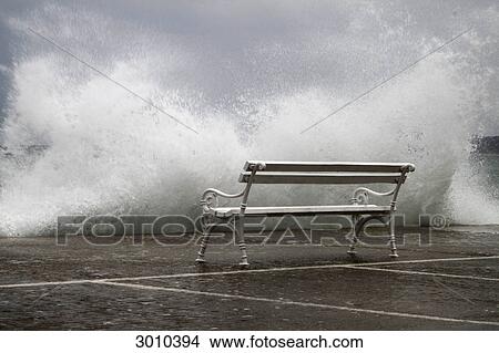 Unoccupied bench in front of massive wave chrashing against quay wall, Vodice, Croatia View Large Photo Image Picture - Unoccupied bench in front of massive wave chrashing against quay wall, Vodice, Croatia . Fotosearch