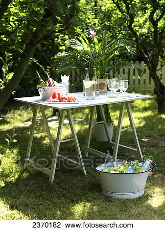 Stock Image - Watermelon slices with beverages and potted plant on table in garden . Fotosearch