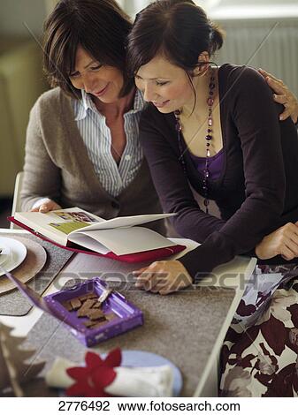 Woman and her daughter reading book at table View Large Photo Image Stock Image - Woman and her daughter reading book at table . Fotosearch