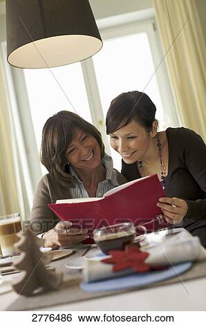 Stock Photograph - Woman and her daughter reading book at breakfast table . Fotosearch