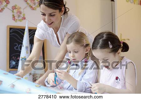 Stock Image - Woman helping her two daughters to decorate cardboard cone . Fotosearch
