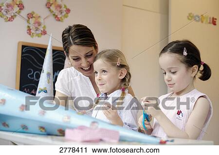 Woman helping her two daughters to decorate cardboard cone View Large Photo Image Stock Image - Woman helping her two daughters to decorate cardboard cone . Fotosearch