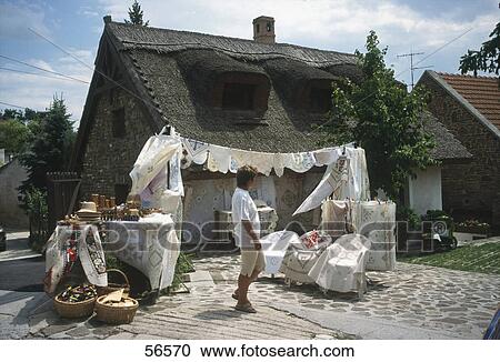 Stock Image - Woman looking at crocheted clothing for sale in front of house, Hungary . Fotosearch
