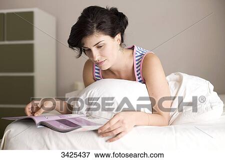 Woman reading a magazine on bed, low angle view View Large Photo Image Stock Photo - Woman reading a magazine on bed, low angle view . Fotosearch