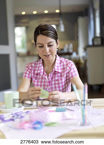 Stock Image - Woman sitting at table and holding card . Fotosearch