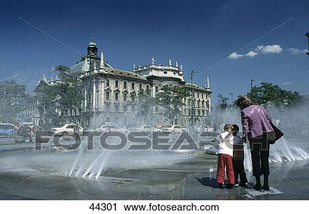 Stock Image - Woman with children near fountain in front of Justice Palace, Karlsplatz, Munich, Bavaria, Germany . Fotosearch
