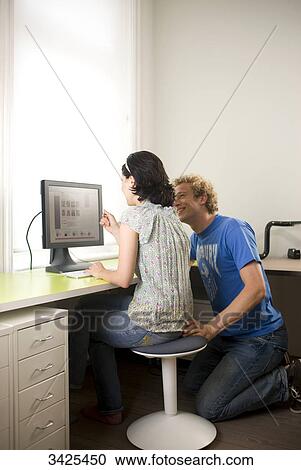 Stock Image - Young couple sitting at desk in front of a computer . Fotosearch