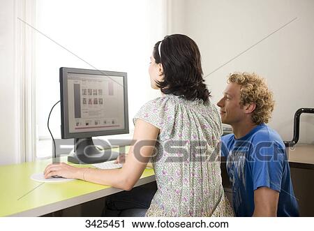Young couple sitting at desk in front of a computer View Large Photo Image Stock Image - Young couple sitting at desk in front of a computer . Fotosearch