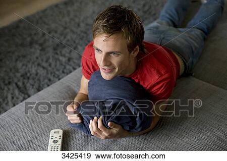 Young man lying on a couch, holding a pillow, elevated view View Large Photo Image Stock Photo - Young man lying on a couch, holding a pillow, elevated view . Fotosearch