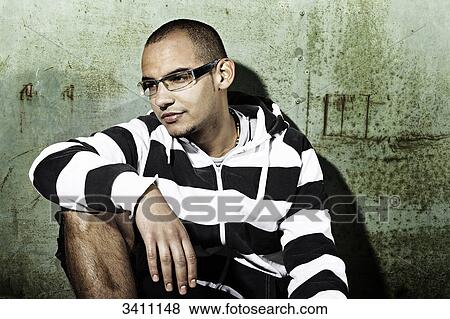 Stock Photo - Young man sitting in front of a gate, portrait . Fotosearch