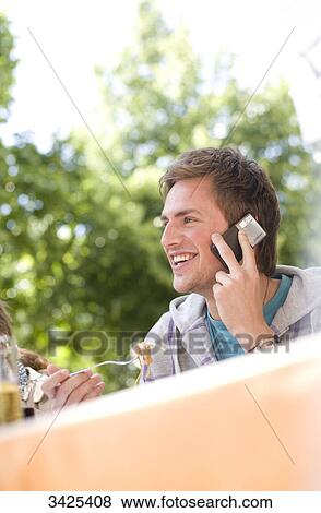 Stock Photo - Young man talking on mobile phone and eating, low angle view . Fotosearch