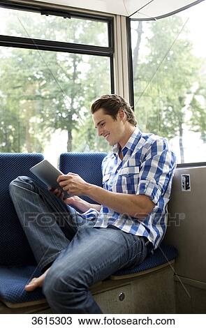 Stock Image - Young man using iPad in tram . Fotosearch