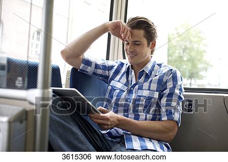 Stock Photograph - Young man using iPad in tram . Fotosearch