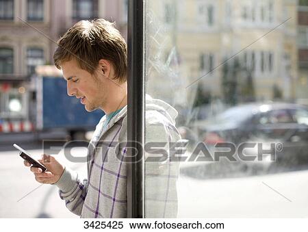 Young man using mobile phone at bus stop, side view View Large Photo Image Stock Photography - Young man using mobile phone at bus stop, side view . Fotosearch