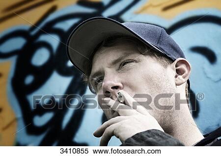 Stock Photography - Young man with cigarette and cap in front of graffiti wall . Fotosearch