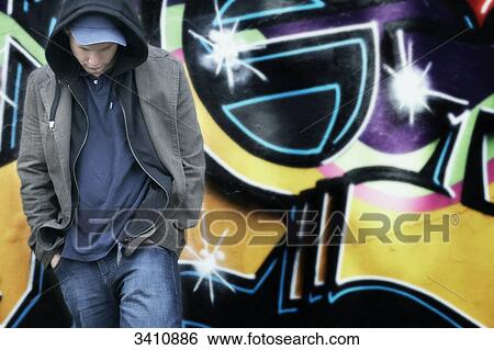 Young man with hooded jacket and cap in front of a graffiti wall View Large Photo Image Stock Photograph - Young man with hooded jacket and cap in front of a graffiti wall . Fotosearch