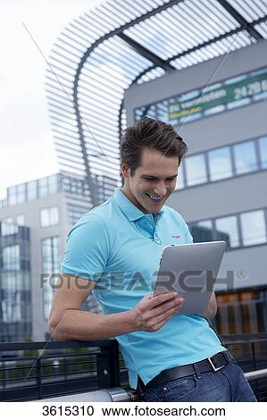 Stock Image - Young man with iPad in front of office building . Fotosearch