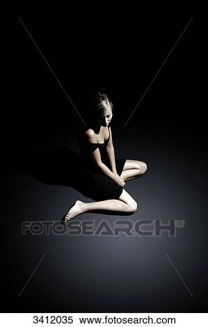 Stock Photography - Young woman in black dress sitting on floor . Fotosearch
