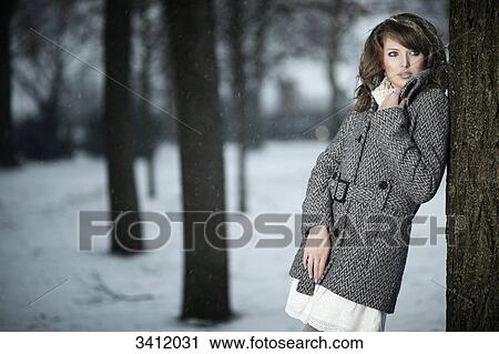 Stock Image - Young woman leaning against tree . Fotosearch