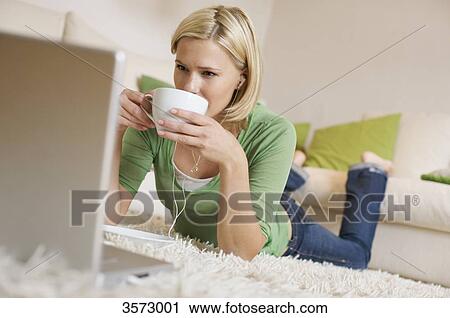 Young woman lying on rug with cup of coffee, earbuds and laptop View Large Photo Image Stock Image - Young woman lying on rug with cup of coffee, earbuds and laptop . Fotosearch