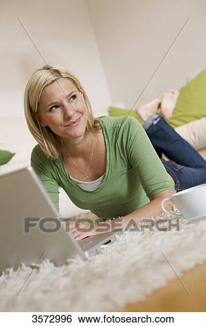 Young woman lying on rug with cup of coffee, earbuds and laptop View Large Photo Image Stock Photograph - Young woman lying on rug with cup of coffee, earbuds and laptop . Fotosearch