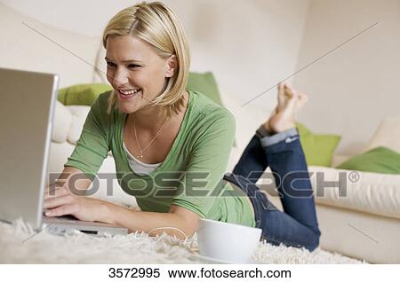 Young woman lying on rug with cup of coffee, earbuds and laptop View Large Photo Image Stock Photography - Young woman lying on rug with cup of coffee, earbuds and laptop . Fotosearch