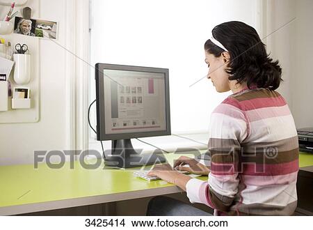 Picture - Young woman sitting at desk and working with computer . Fotosearch